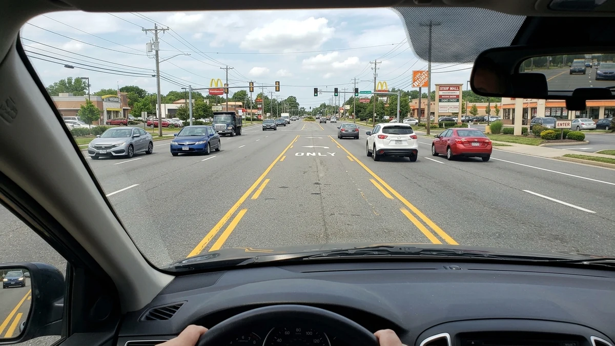 Cockpit view of a vehicle positioned inside a center two-way left-turn lane with yellow dashed inner markings preparing to make a left turn
